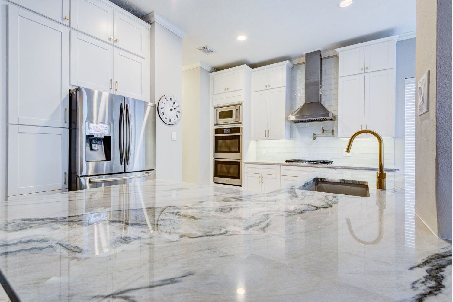 marble countertop kitchen island with a gold faucet in a houston kitchen remodel with white cabinets and stainless steel appliances