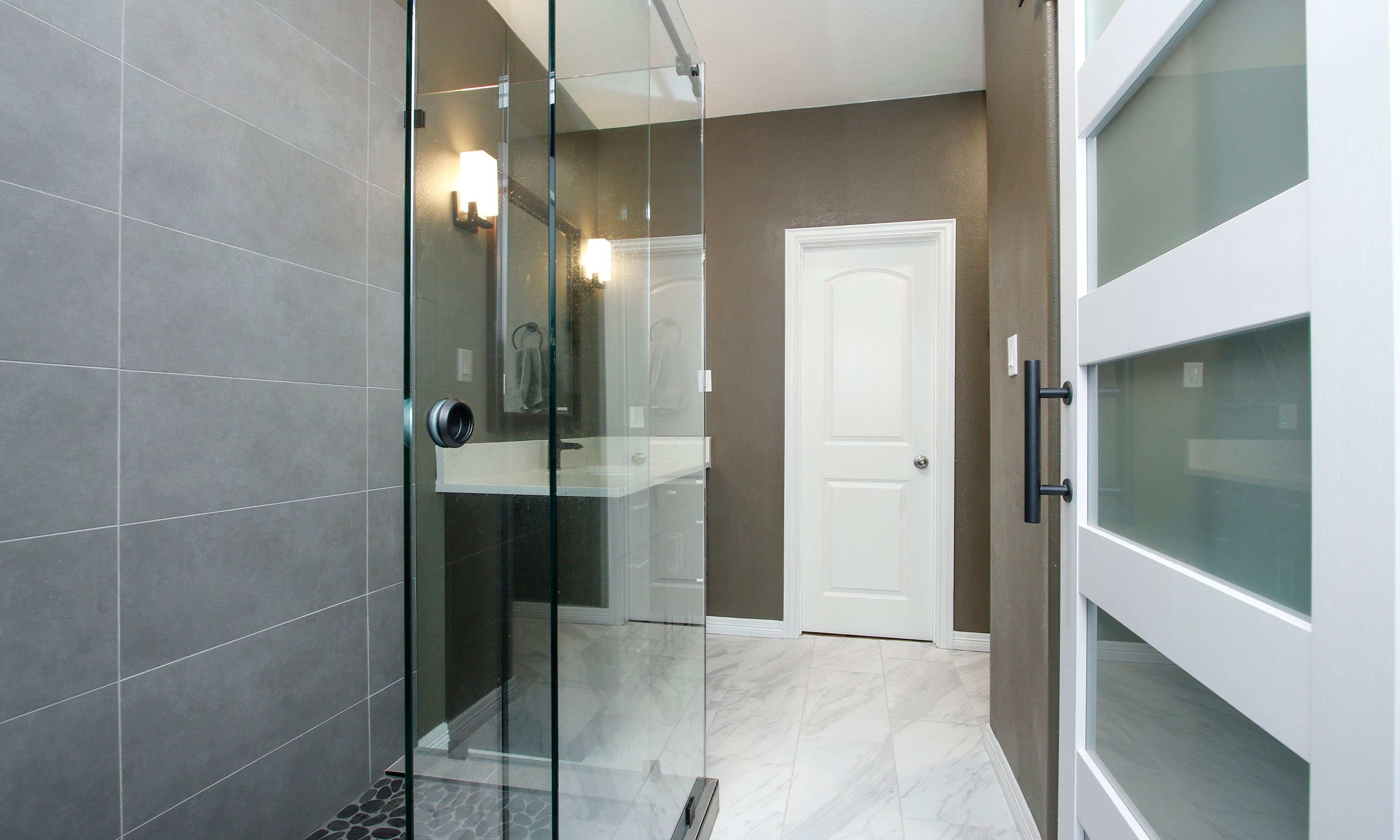 texas bathroom remodel with large gray shower tiles, brown walls, and light marble floor tiles